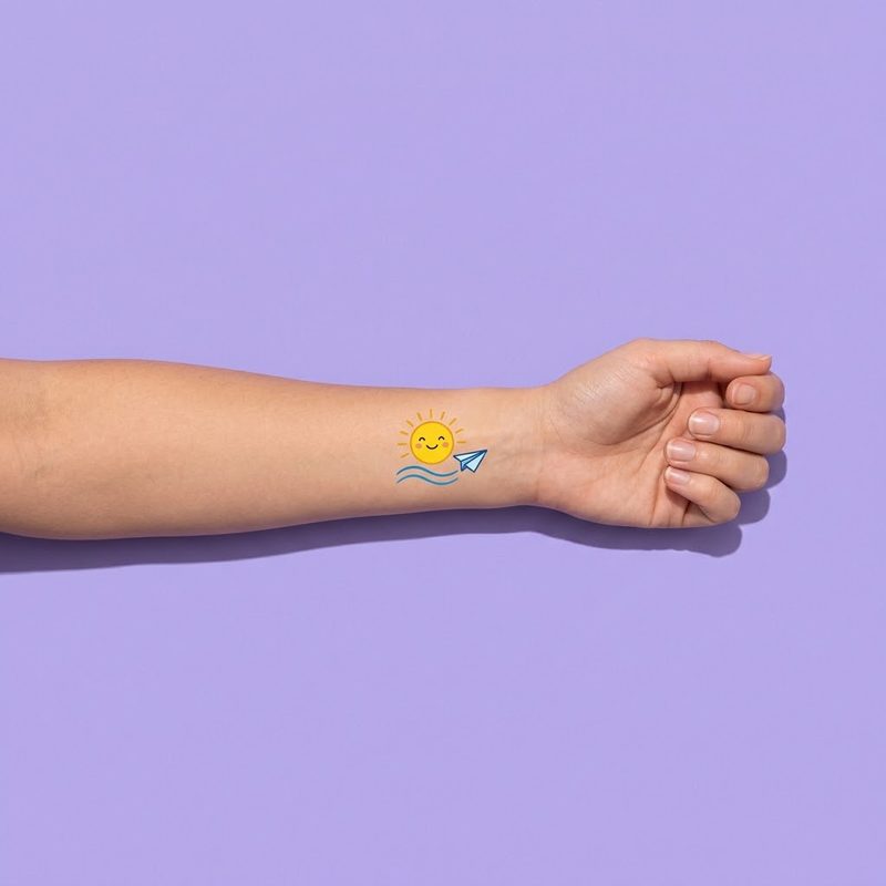 A forearm printed with a small sun, waves and a paper plane